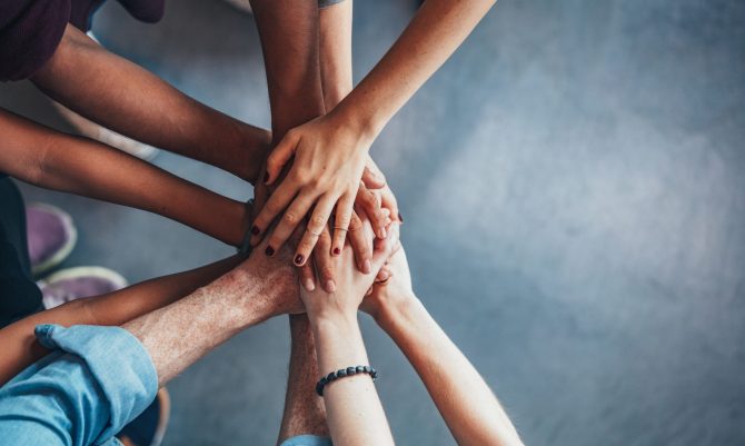 Close up top view of young people putting their hands together. Friends with stack of hands showing unity and teamwork.